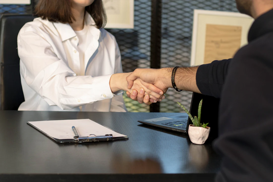 Two people shaking hands across a desk after agreeing a deal